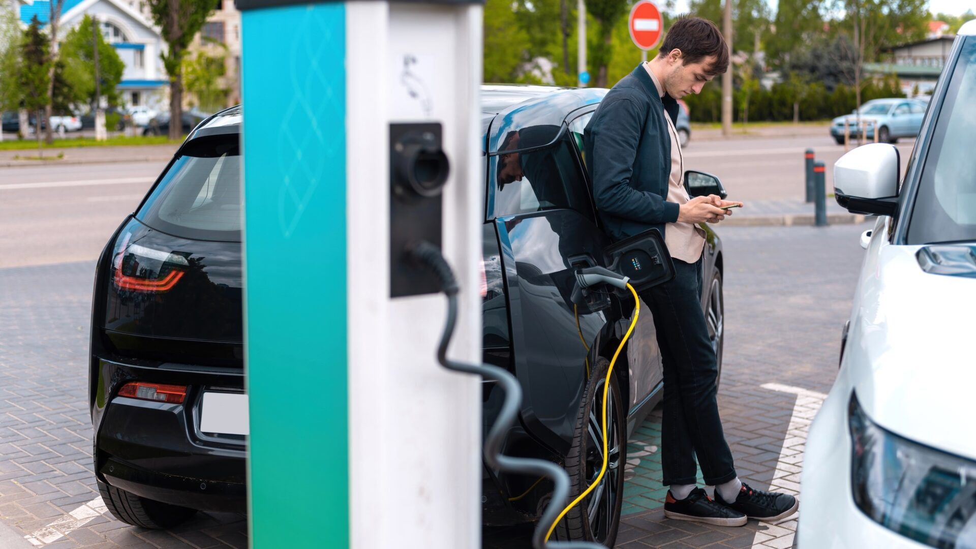 Un homme charge sa voiture électrique à la station de charge et l'utilisation du smartphone