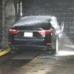 Une voiture noire nettoyée dans un lavage automatisé avec de l'eau et de la mousse.