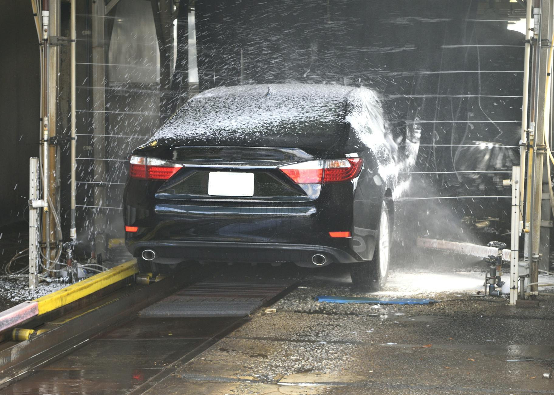 Une voiture noire nettoyée dans un lavage automatisé avec de l'eau et de la mousse.