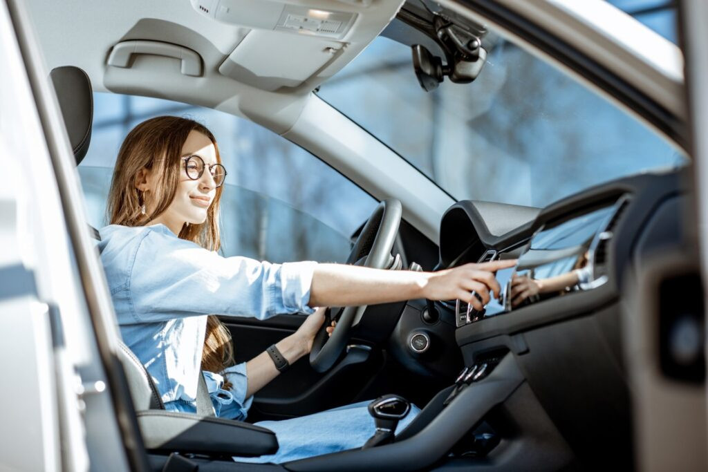 Jeune femme touchant un moniteur de voiture tout en étant assis dans la voiture moderne de la ville