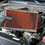 Un mécanicien automobile portant des gants de travail de protection contient un filtre à air sale et bouché sur un moteur de voiture pendant la maintenance automatique.