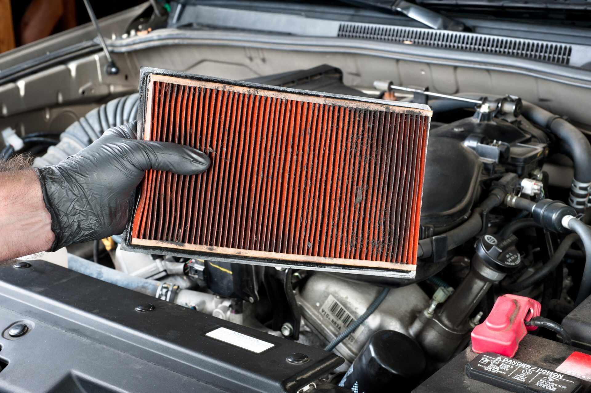 Un mécanicien automobile portant des gants de travail de protection contient un filtre à air sale et bouché sur un moteur de voiture pendant la maintenance automatique.