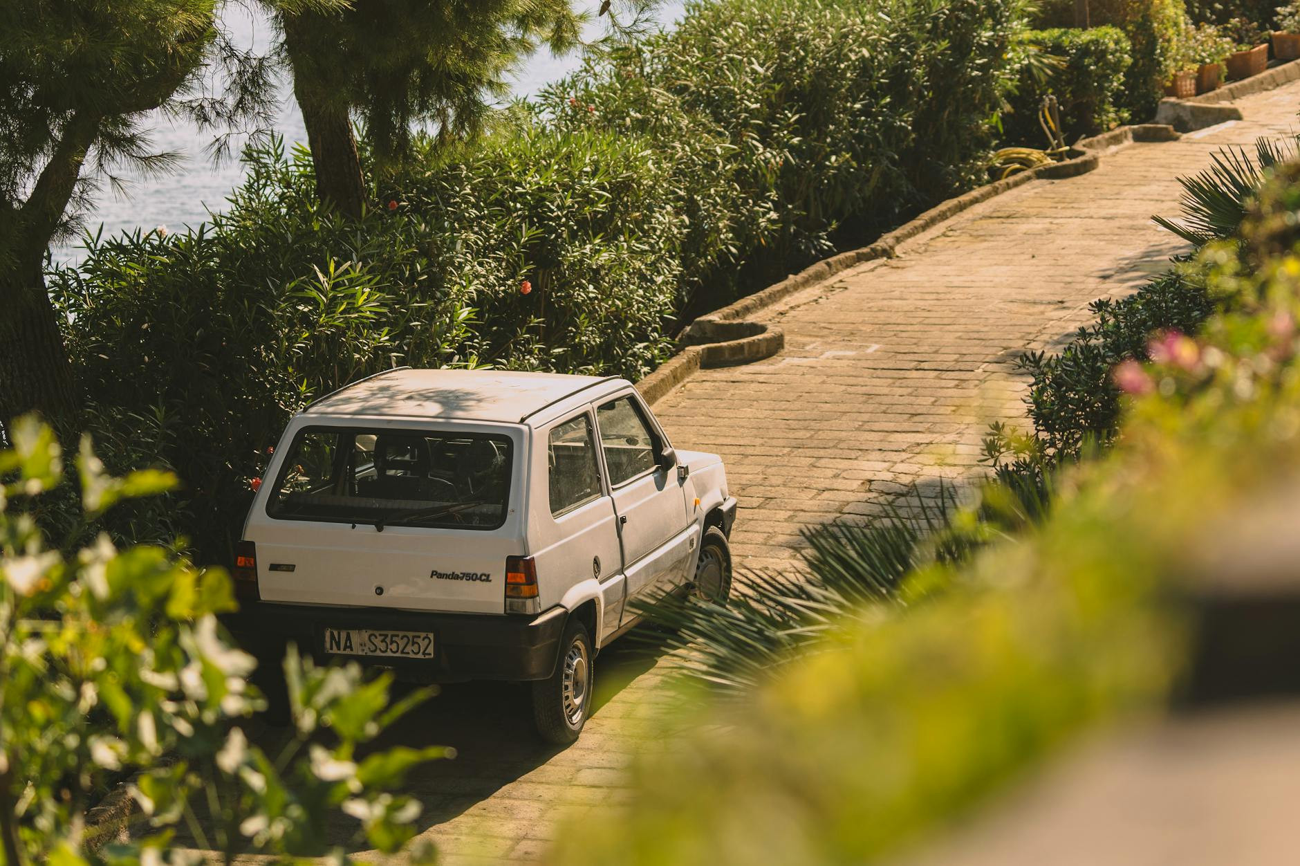 Un panda de fiat blanc sur un chemin pavé serein entouré de verdure à Naples, en Italie.