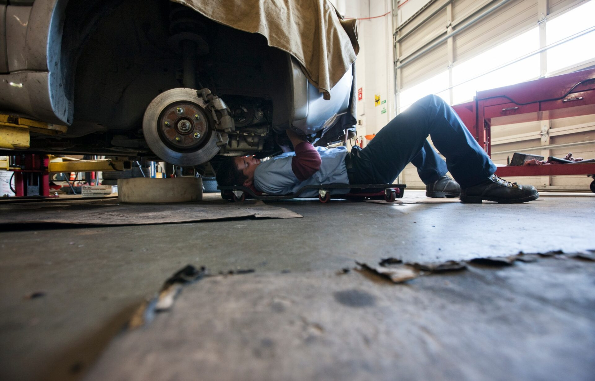 Le mécanicien se trouve sur un chariot sous une voiture dans un atelier de réparation automobile