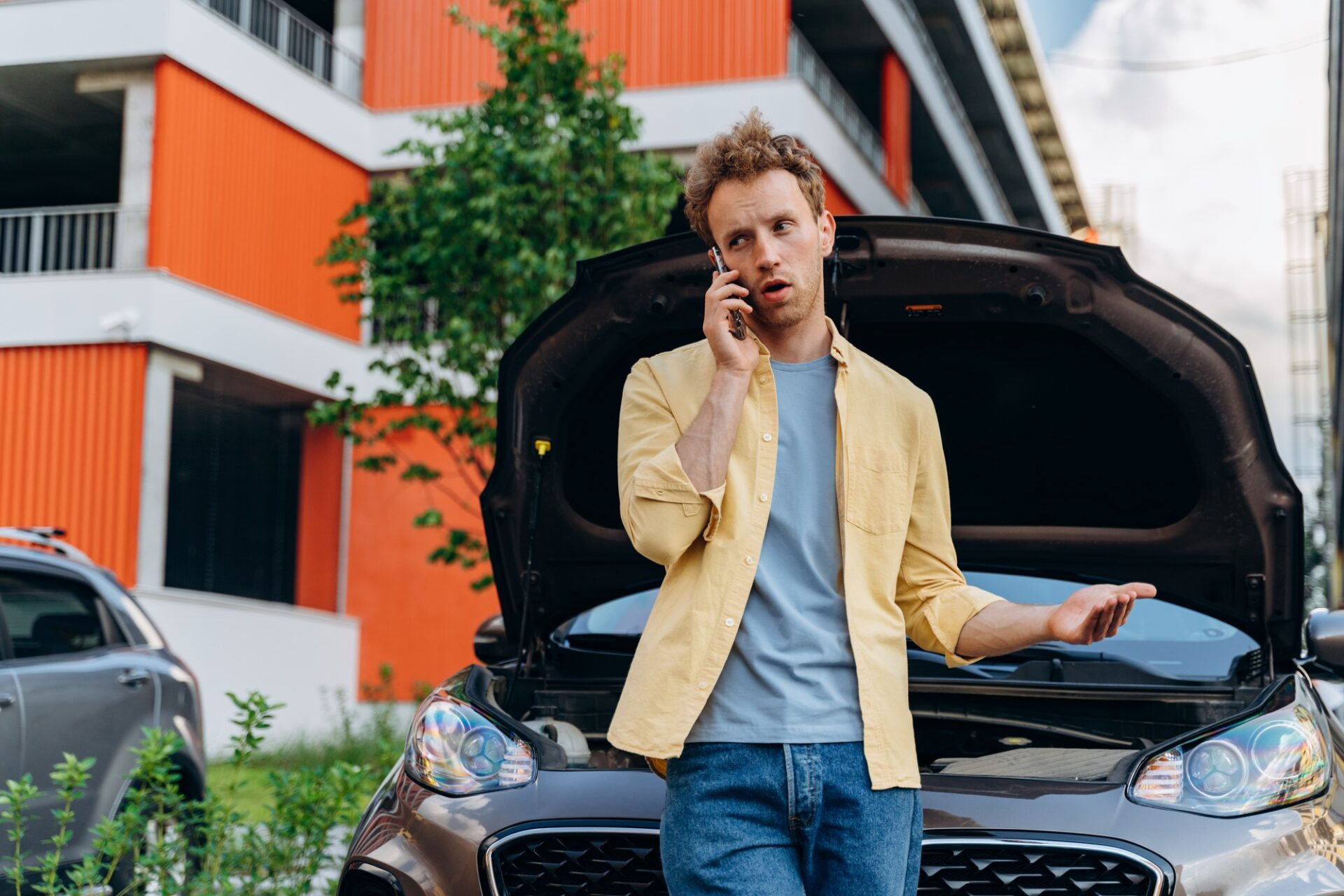 Close Up Portrait d'un jeune homme ayant des problèmes avec sa voiture détruite, ouvrant le capot et appelant à l'aide sur un téléphone mobile.