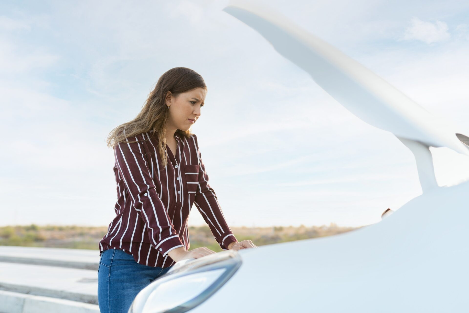 Jeune femme caucasienne avec son capot de voiture ouverte et en regardant le moteur en panne avec une expression triste et confuse