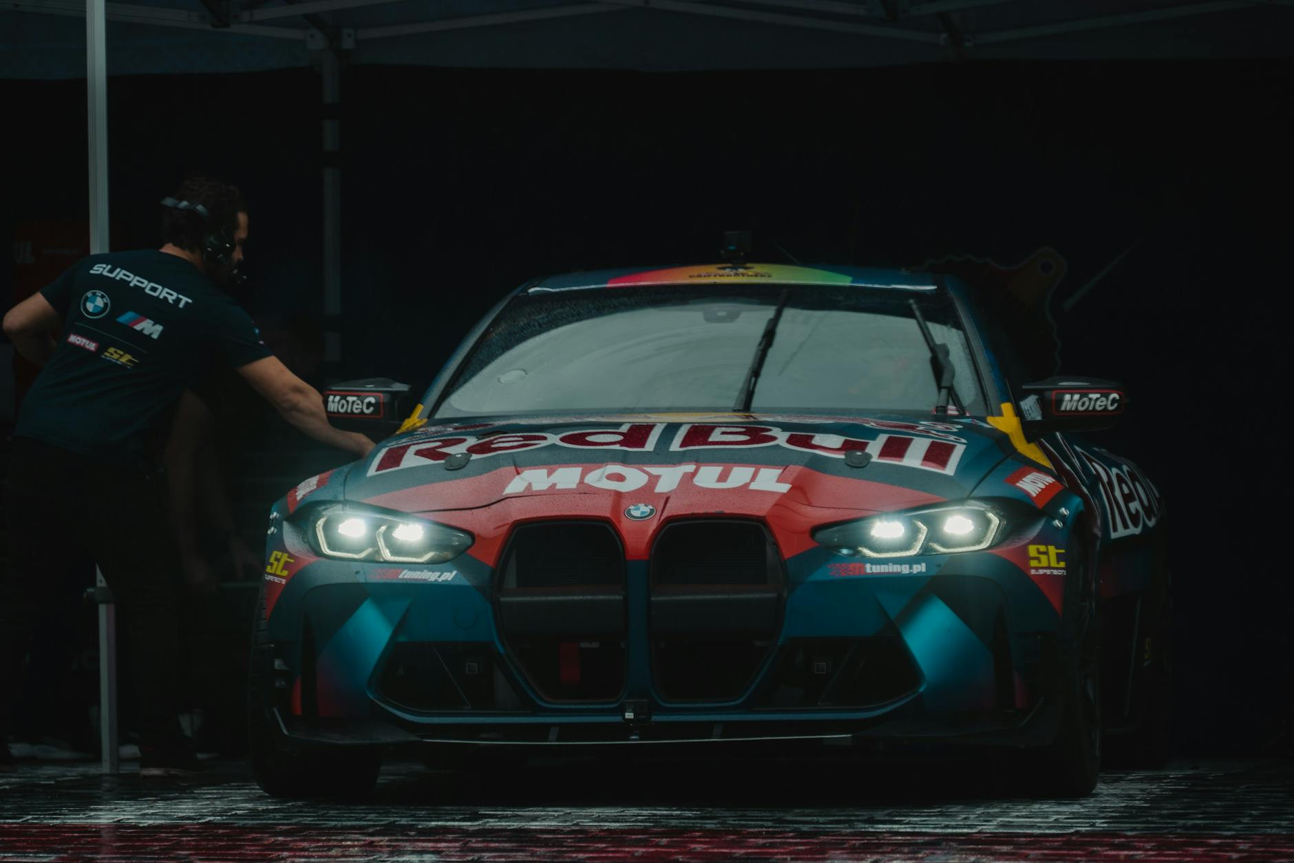 Vue de face d'une voiture de course BMW M4 arborant la marque Red Bull Motul sous un éclairage tamisé.